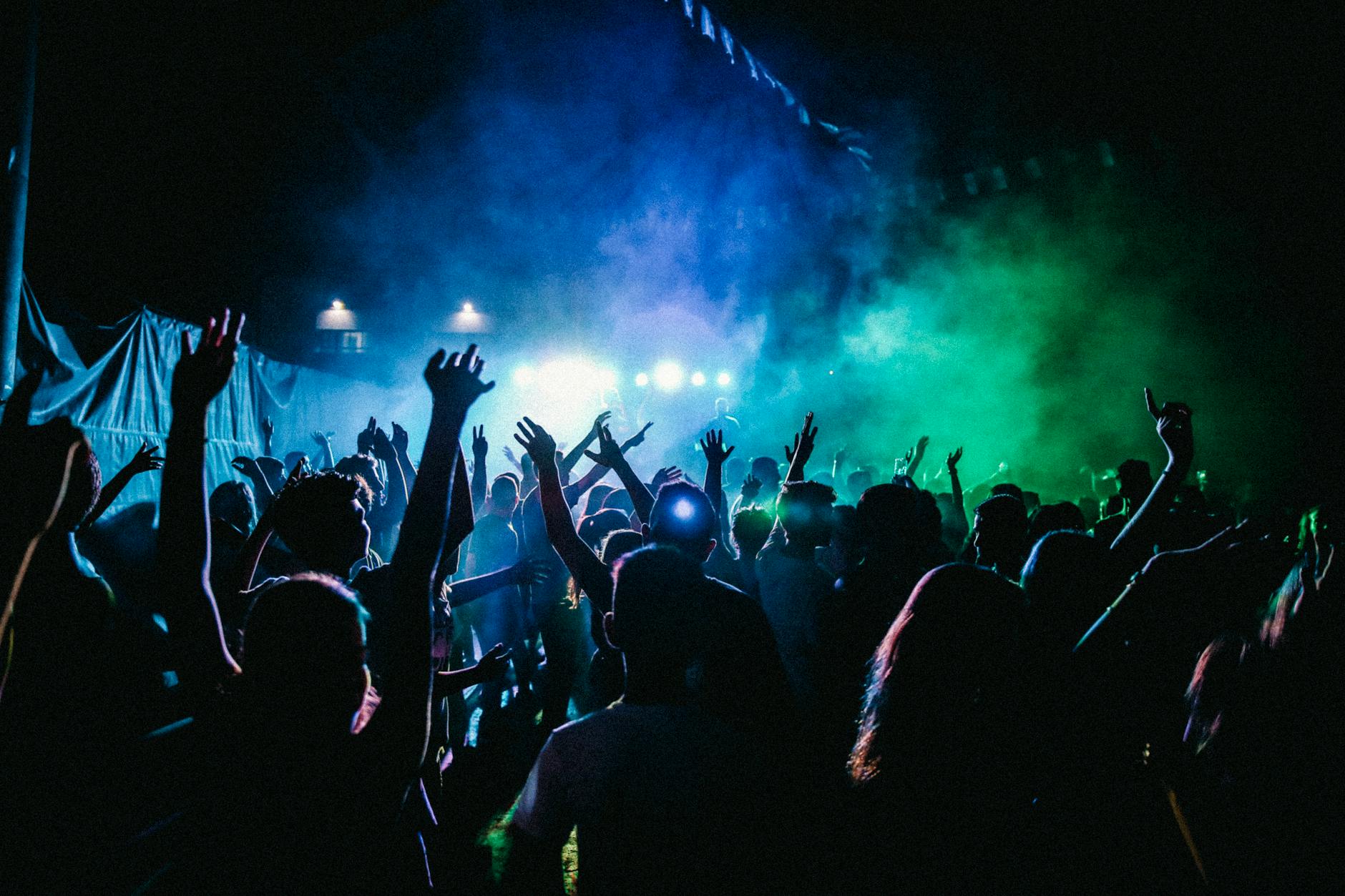 people raising their hands in front of stage with lights