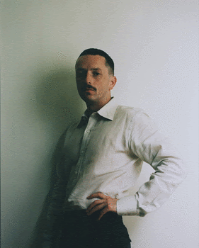 a man with a mustache and a mustache standing against a wall